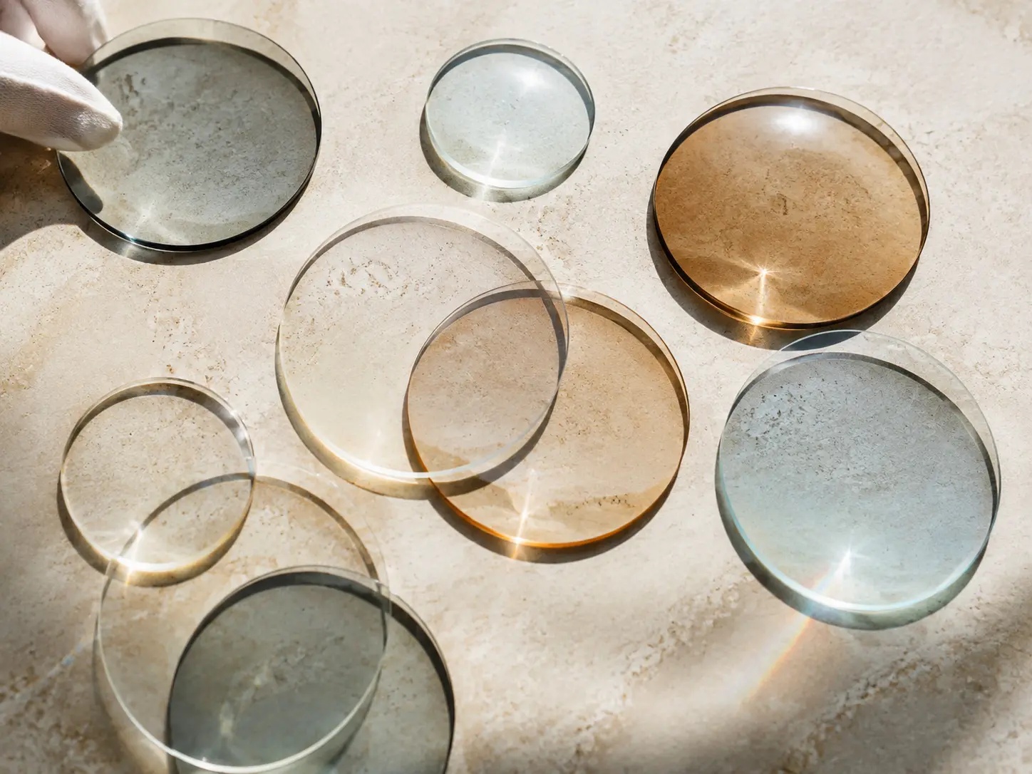 Loose round optical lenses casting overlapping circular shadows on cream stone